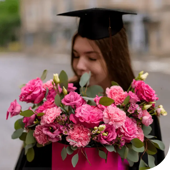 A graduate smiles while holding a bouquet of pink flowers, representing BloomNation’s marketplace success supported by Peak Support’s back office expertise in tasks like design, data entry, and customer onboarding. Peak Support is a customer experience partner dedicated to your growth.